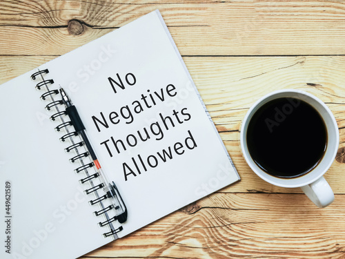Open notebook with text "No Negative Thoughts Allowed" and a cup  of coffee on wooden background.