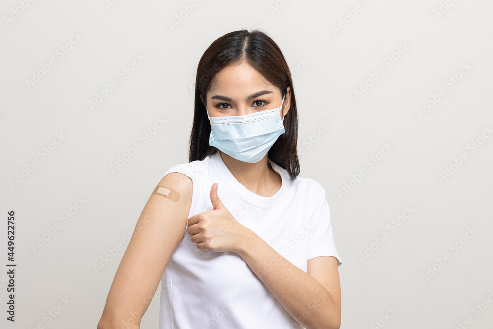 Young beautiful asian woman wearing mask and getting a vaccine protection the coronavirus. Happy female showing arm with bandage after receiving vaccination on isolated white background. Young beautiful asian woman wearing mask and getting a vaccine protection the coronavirus. Happy female showing arm with bandage after receiving vaccination on isolated white background.