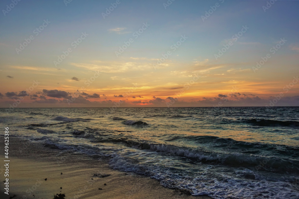 Dawn over the Caribbean Sea. The sky above the horizon is highlighted in orange. The surf waves are foaming on the sandy beach. Mexico 