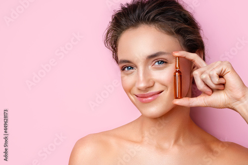 Woman holds ampoule with serum for hair or skin care. Photo of attractive woman with perfect makeup on pink background. Beauty concept