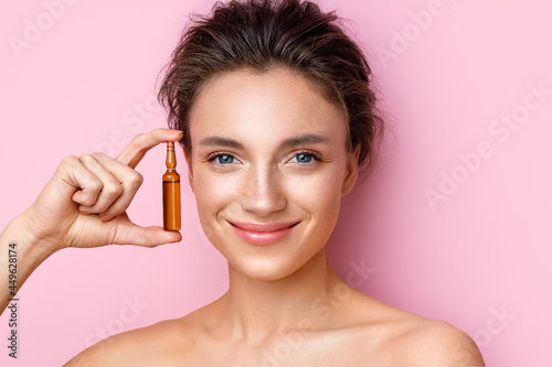 Woman holds ampoule with serum for hair or skin care. Photo of attractive woman with perfect makeup on pink background. Beauty concept photo