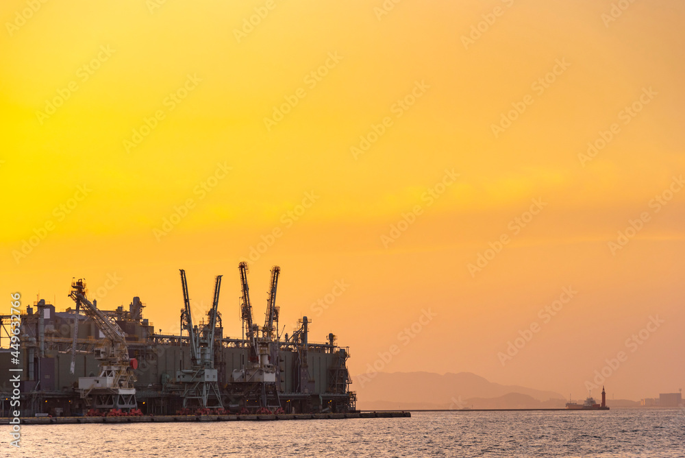 Dock industry cranes silhouette in container terminal port with golden sunset sky with clouds
