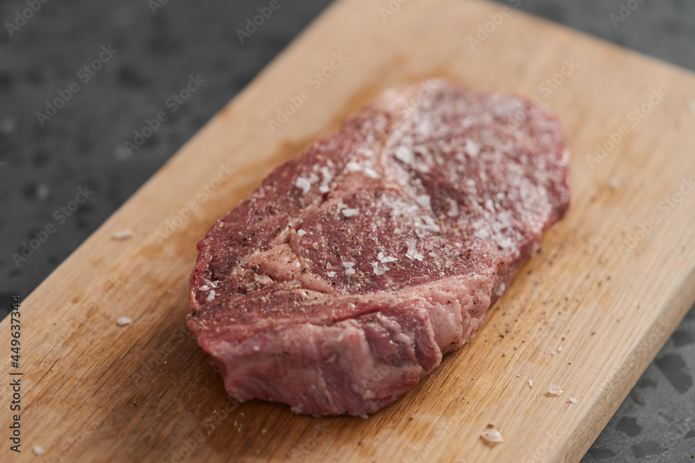 Raw ribeye steak spiced and ready to cook on oak board