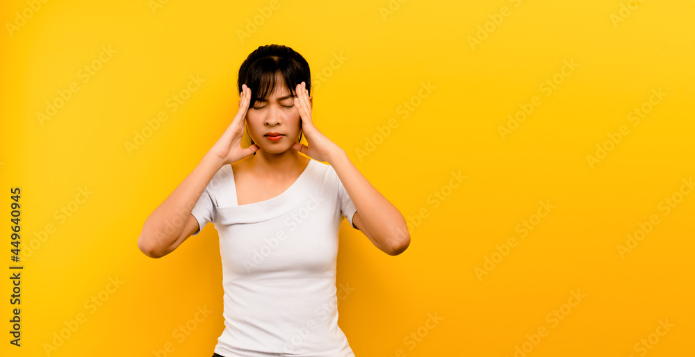 Portrait of an Asian girl Hands touching temples, feeling stressed, having a headache. dizziness due to stress on a yellow background Portrait of an Asian girl Hands touching temples, feeling stressed, having a headache. dizziness due to stress on a yellow background