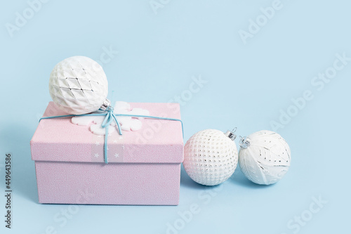 Pink Christmas gift box with white baubles on baby blue. Merry Christmas or Happy New Year greeting card with copy space with snow bokeh lights