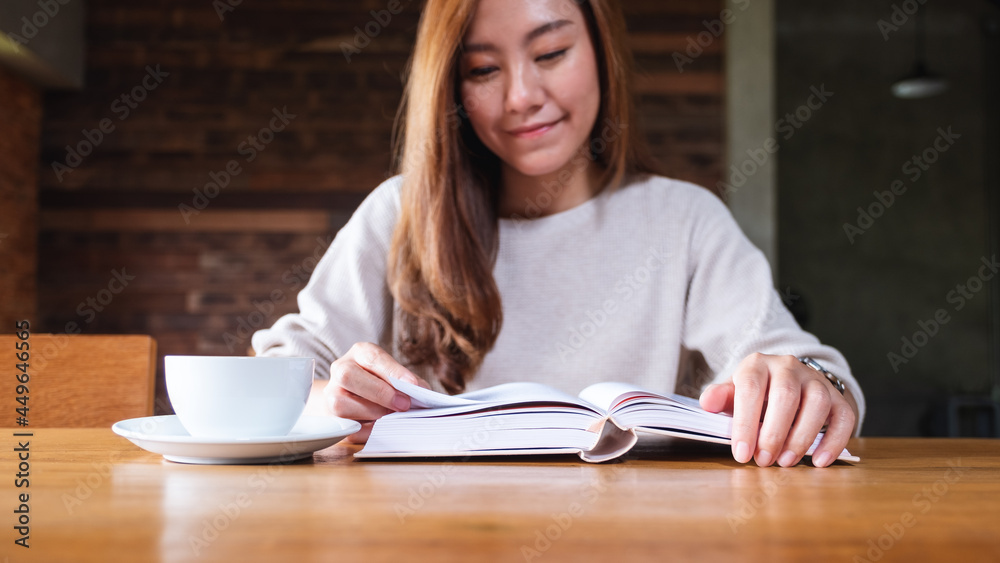 Obraz premium Closeup image of a beautiful asian woman holding and reading a book with coffee cup on the table