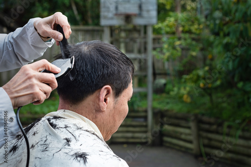 A man is getting a home haircut by his wife in the backyard – stay home, self isolation concept.