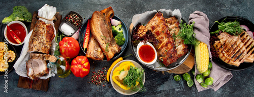 Assortment of grilled pork meat with vegetables on dark grey background.