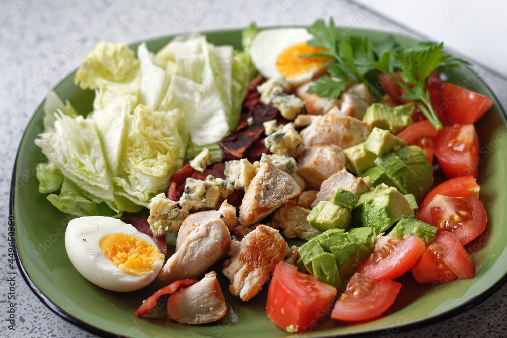 A colourful cobb salad freshly prepared on a green plate