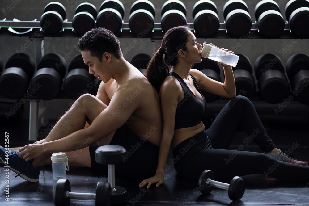 Fit Asian couple break of dumbbell workout in gym