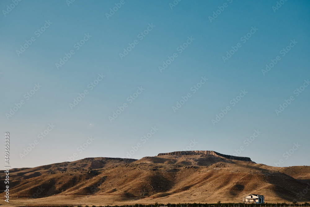 Naklejka premium A single house behind the agricultural field and small hill with shadows on hills during sunset. Natural view of middle side of Turkey