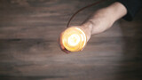 Male hand holding light bulb over wooden background.