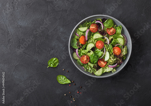 Fresh healthy vegetarian vegetables salad with tomatoes and cucumber, red onion and spinach in grey bowl plate on dark background.
