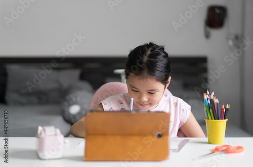 asian child student back to school or kid girl smile write or drawing and coloring with computer tablet to learning or people learn from home in bedroom and colour pencils on desk for art study online