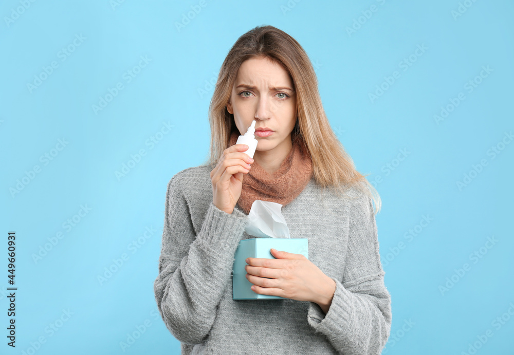 Sick young woman using nasal spray on light blue background Sick young woman using nasal spray on light blue background