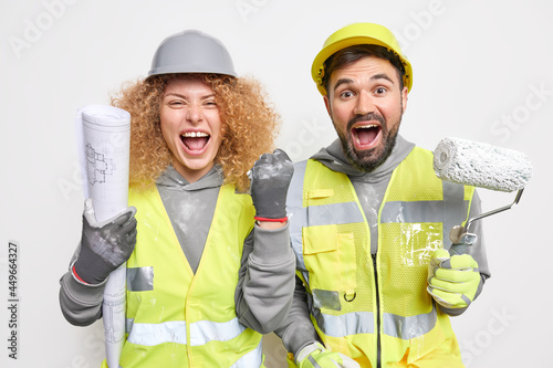 Emotional woman and man construction workers exclaim loudly work on home apartment interior clench fist satisfied with results hold painting roller and architectural blueprint. Engineering concept photo