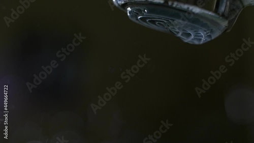 Backlit water stream running from a tap against a black background, close up. photo