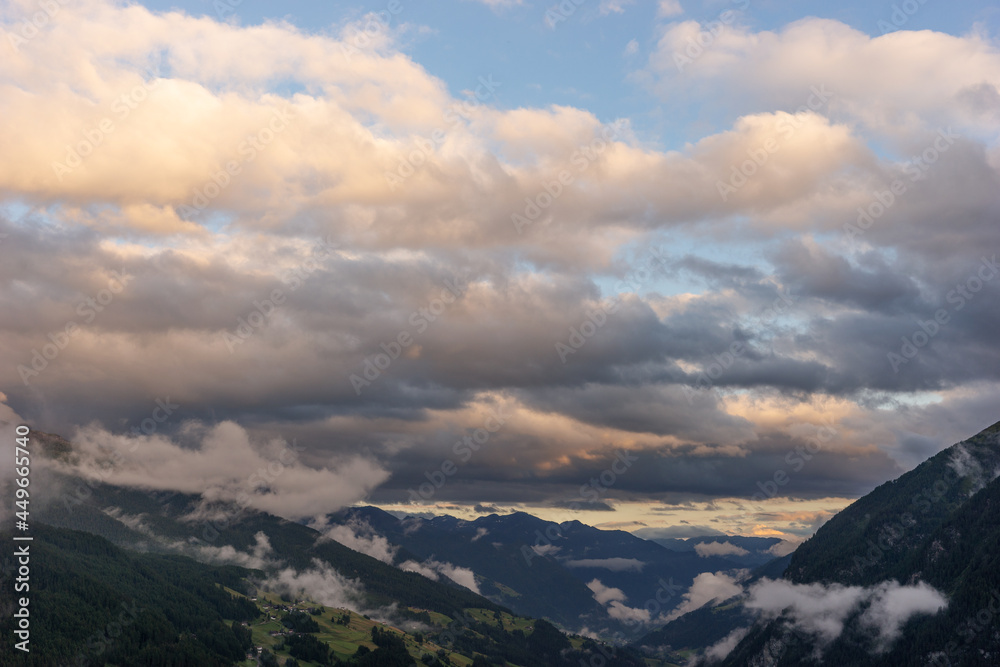 Silhouettes of mountains on sunset. Clouds over the valley in the Alps