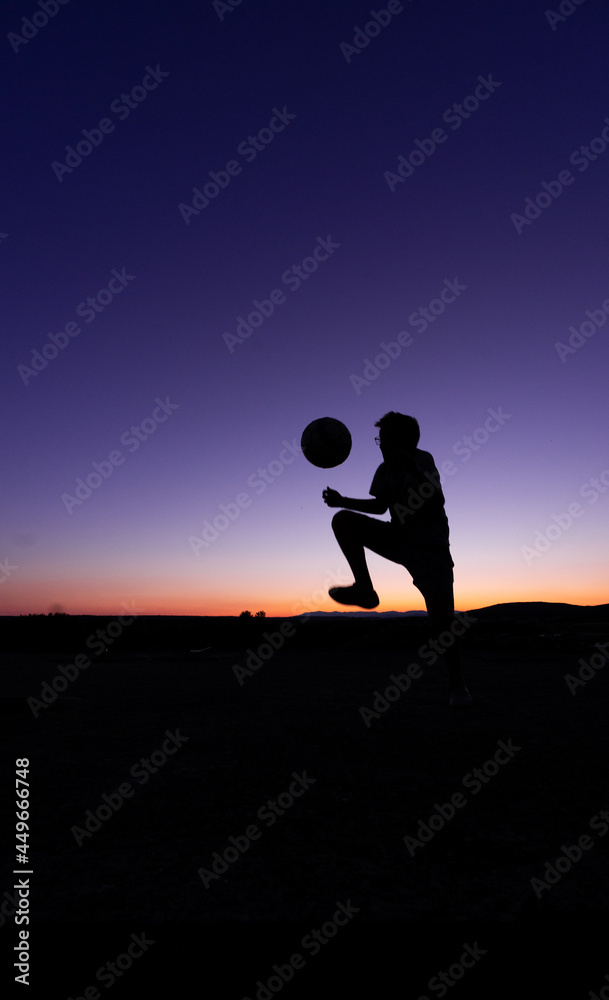 SILHOUETTE OF A BOY PLAYING BALL AT SUNSET