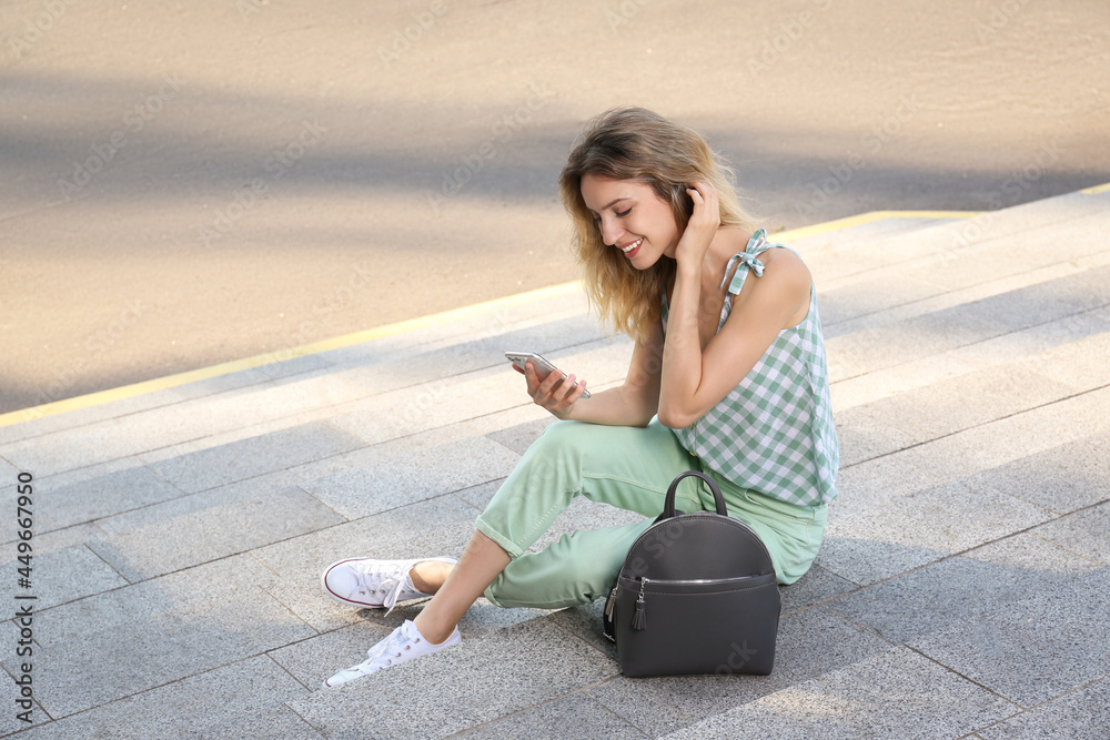 Young woman with stylish backpack and smartphone on stairs outdoors