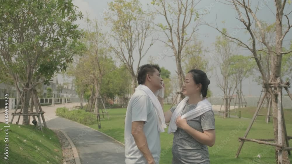 Slow motion happy Asian senior couple wife wiping sweat from husband face after running or jogging at the village outdoor park. Senior couple romantic moment Slow motion happy Asian senior couple wife wiping sweat from husband face after running or jogging at the village outdoor park. Senior couple romantic moment