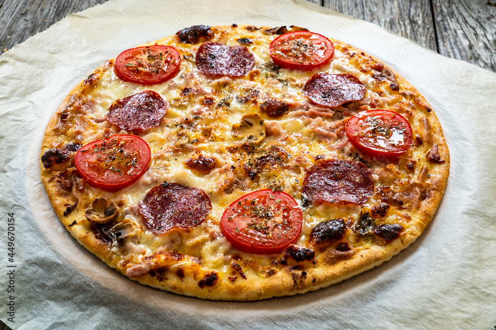 Circle pepperoni pizza with mozzarella, salami and tomatoes on wooden table
