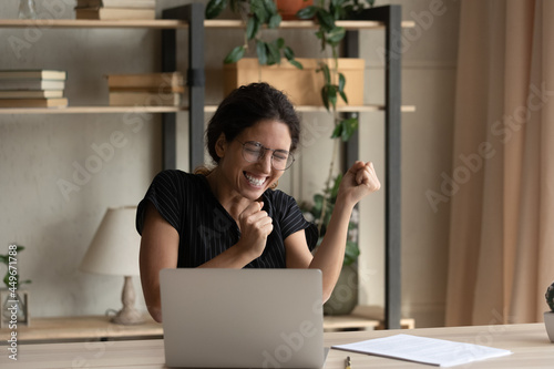 Close up overjoyed businesswoman in glasses celebrating success, yes gesture, using laptop, sitting at desk, excited woman received good news in message, project results, student get scholarship photo