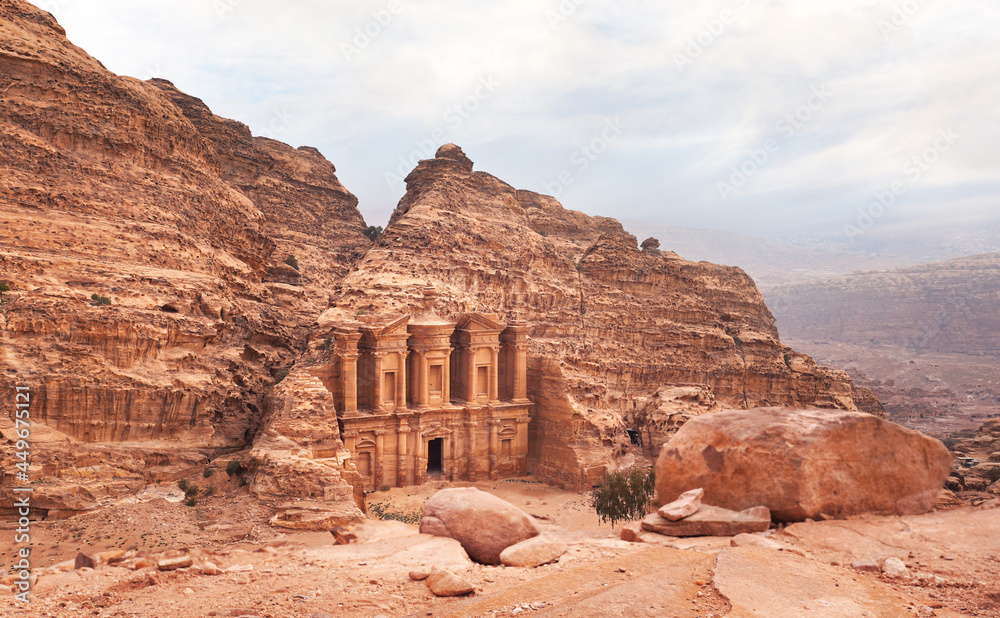 Ad Deir - Monastery - ruins carved in rocky wall at Petra Jordan, mountainous terrain with overcast sky background Ad Deir - Monastery - ruins carved in rocky wall at Petra Jordan, mountainous terrain with overcast sky background