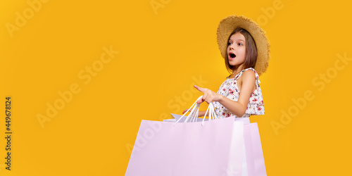 Portrait Of Joyful Teen Girl In Straw Hat With Bright Shopping Bags Over Yellow Background, Copy Space