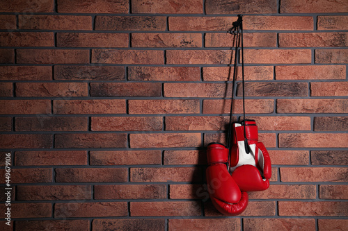 Pair of red boxing gloves hanging on brick wall, space for text © New Africa