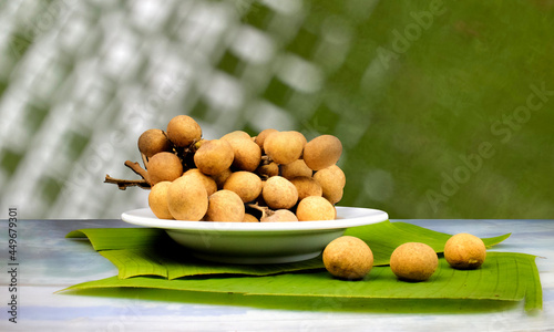 longan is a famous tropical fruit of asia in white plate over banana leaf on table,