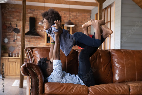 Overjoyed young African American father and teen daughter have fun together in living room at home. Smiling biracial dad play with excited little teenage girl child on weekend. Parenthood concept.