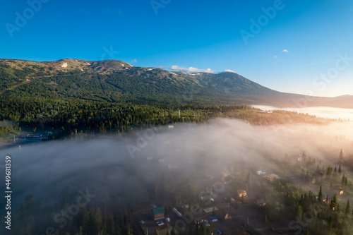 Mountain with visible silhouettes forest tree through morning colorful fog sunrise, aerial top view