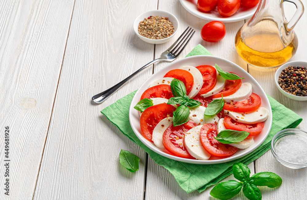 Delicious caprese salad with ripe tomatoes and mozzarella cheese, basil and olive oil on a white background. Italian cuisine.