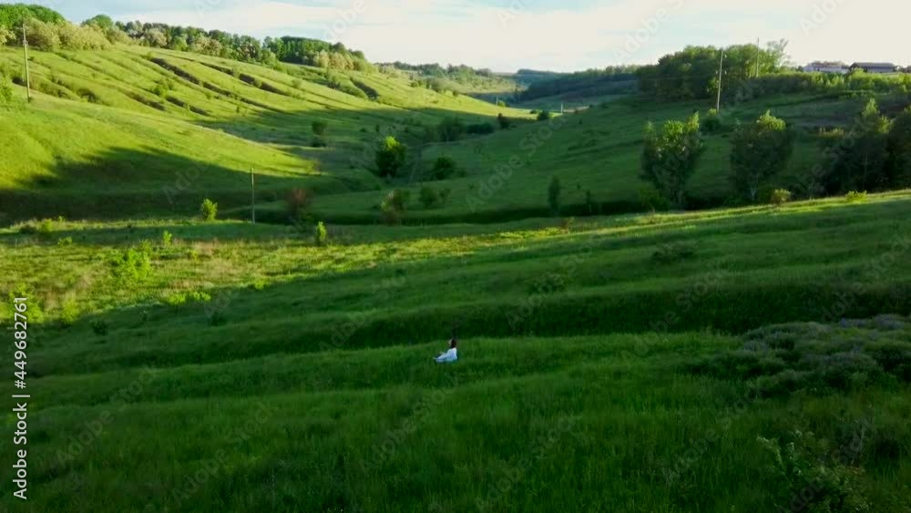 Aerial shot from flying drone of woman in white dress. young girl runs in green grass on an endless field in summer on sunny day. Freedom of man and nature. Top view of young woman traveler on field Aerial shot from flying drone of woman in white dress. young girl runs in green grass on an endless field in summer on sunny day. Freedom of man and nature. Top view of young woman traveler on field