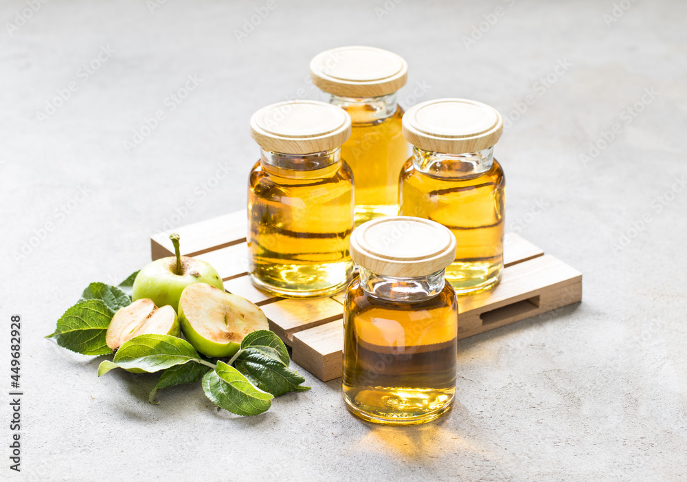 Fresh apple juice in small glass bottles with lids on a wooden pallet on a light gray background Fresh apple juice in small glass bottles with lids on a wooden pallet on a light gray background
