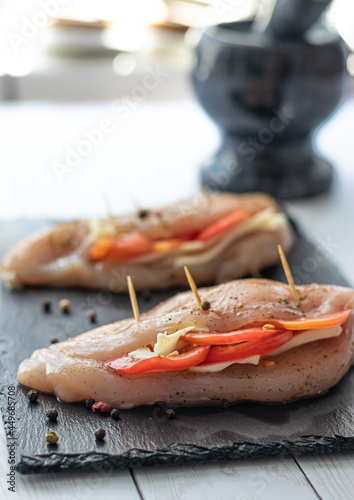 Raw chicken meat cooking with tomatoes,herbs and cheese on black slate board. Chicken fillet. Homemade recipe cook.