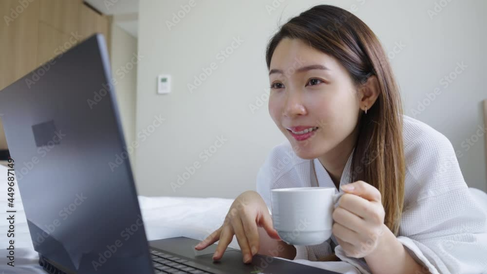 Portrait of Asian woman wearing bathrobe using a laptop while have a morning coffee on bed in bedroom Portrait of Asian woman wearing bathrobe using a laptop while have a morning coffee on bed in bedroom