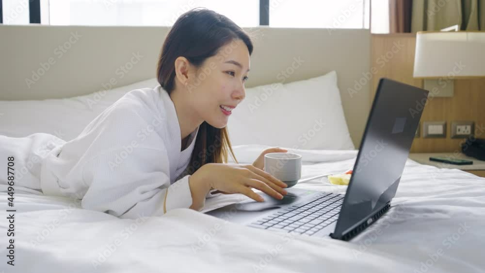 Portrait of Asian woman wearing bathrobe using a laptop while have a morning coffee on bed in bedroom Portrait of Asian woman wearing bathrobe using a laptop while have a morning coffee on bed in bedroom