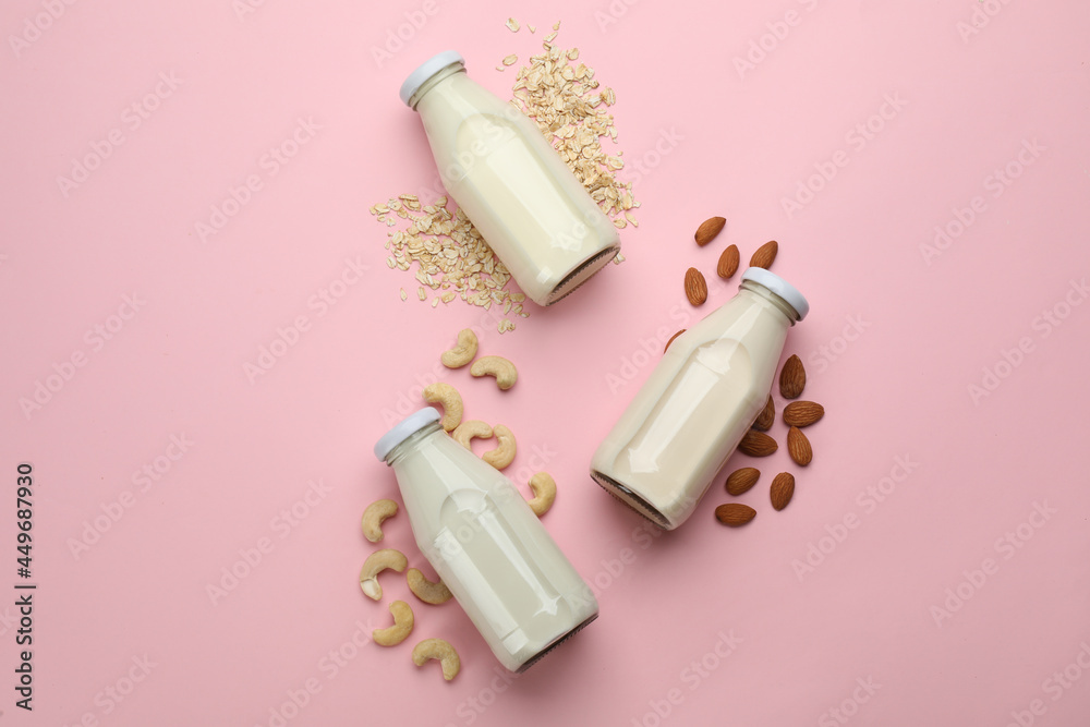 Different vegan milks, oat flakes and nuts on pink background, flat lay Different vegan milks, oat flakes and nuts on pink background, flat lay