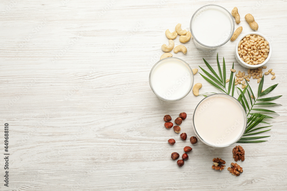 Different vegan milks and nuts on white wooden table, flat lay. Space for text Different vegan milks and nuts on white wooden table, flat lay. Space for text