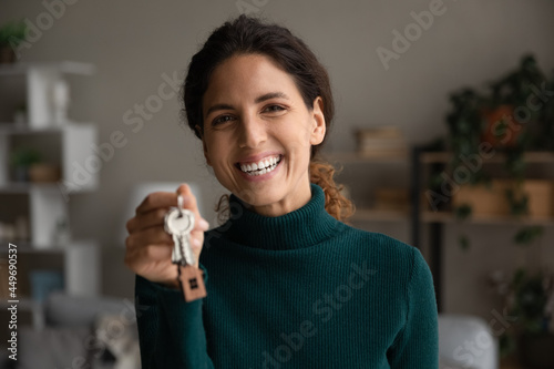 Head shot portrait smiling woman showing keys at camera, purchasing new house, moving into first new apartment, happy young female tenant renter rejoicing relocation, mortgage or rent concept photo