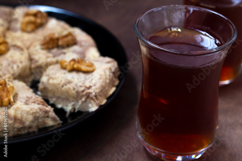 close-up sunflower halva with fork and Turkish tea in traditional glass on the wooden table close-up. glass cup of black tea with walnuts on the dark brown background with copy space.Turkish desserts.