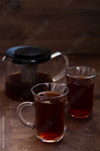 Turkish tea in traditional glass on the wooden table close-up. two glass cups of black tea with teapot on the dark brown background with copy space. vertical
