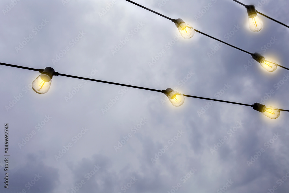 Glowing Light bulbs hanging against the dark evening sky, in a row modern decoration with copy space Glowing Light bulbs hanging against the dark evening sky, in a row modern decoration with copy space