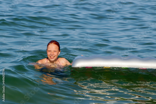 smiling teenage girl swims with inflatable mattress in the sea