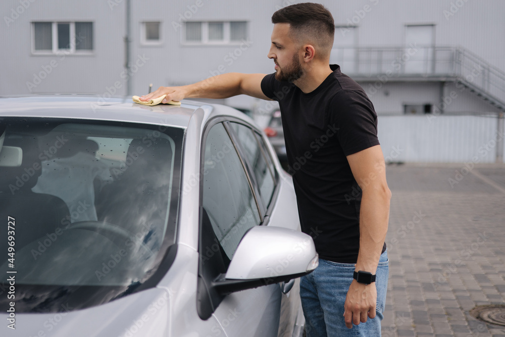 Man wipes a windshield of his car with a rag in a showroom at a self-service car wash Man wipes a windshield of his car with a rag in a showroom at a self-service car wash