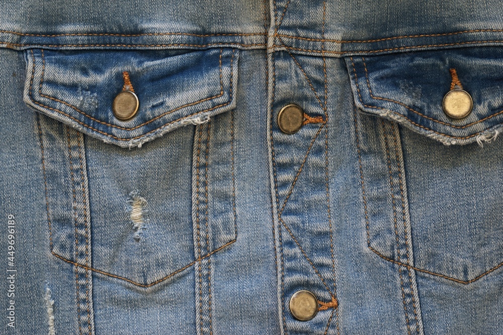 the front part with the upper pockets of an old or worn blue denim jacket is a closeup the front part with the upper pockets of an old or worn blue denim jacket is a closeup