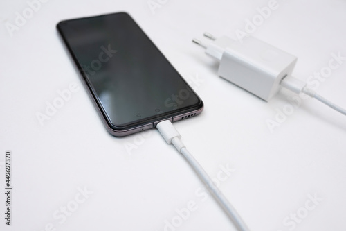 Charging a smartphone via a USB cable on a white background, close up. Silhouette of a black smartphone hanging with a usb charging cable on a white background. Copy space