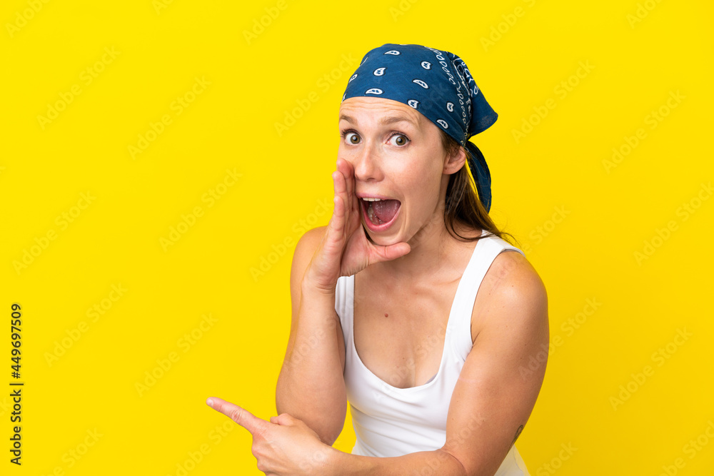 Young English woman isolated on yellow background pointing to the side to present a product and whispering something Young English woman isolated on yellow background pointing to the side to present a product and whispering something
